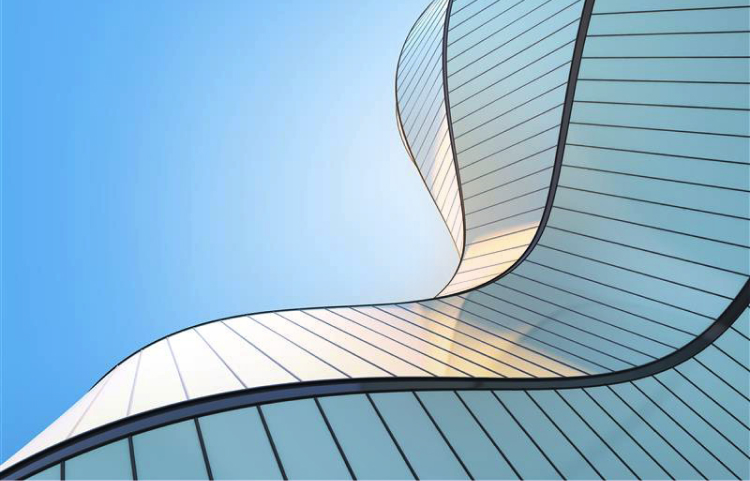 Un bâtiment moderne doté d'une façade en verre élégante et incurvée qui reflète la lumière du soleil sur un ciel d'un bleu profond.